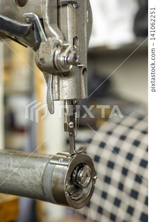 The precise moment in textile manufacturing: the needle and presser foot of a sewing machine sew through the fabric. The precise moment in textile manufacturing: the needle and presser foot of a sewing machine sew through the fabric. 141062251