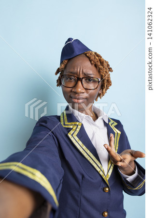 African American woman in flight attendant uniform gesturing and speaking to coworker on camera. Confused black air hostess participating in travel vlog, replying to questions from online audience. 141062324