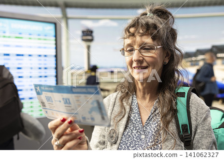 Joyful senior woman standing near terminal window view in airport, smiling and ready for takeoff. Elderly solo traveler symbolizing optimism and modern travel lifestyle during golden years. Joyful senior woman standing near terminal window view in airport, smiling and ready for takeoff. Elderly solo traveler symbolizing optimism and modern travel lifestyle during golden years. 141062327
