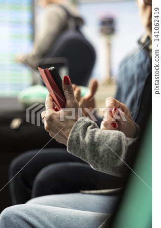 Close up of active elderly couple using smartphone in airport near boarding gate, reviewing schedule and agenda for upcoming trip. Senior couple embracing adventurous retirement life. Close up of active elderly couple using smartphone in airport near boarding gate, reviewing schedule and agenda for upcoming trip. Senior couple embracing adventurous retirement life. 141062419