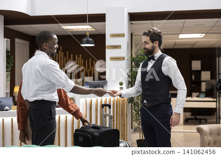 Cash tips, handing banknotes to bellboy, luxury concierge services, hotel staff receives money after assistance with suitcases. Gratitude for worker and tipping culture in the hospitality industry. Cash tips, handing banknotes to bellboy, luxury concierge services, hotel staff receives money after assistance with suitcases. Gratitude for worker and tipping culture in the hospitality industry. 141062456