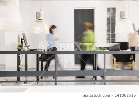 Busy modern office shows diverse employees walking in motion blur, creating sense of fast paced corporate activity. Multiethnic professionals move around workplace, working toward office deadlines. Busy modern office shows diverse employees walking in motion blur, creating sense of fast paced corporate activity. Multiethnic professionals move around workplace, working toward office deadlines. 141062510