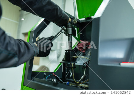 Mechanic hand in glove tightening diesel fuel injector with wrench tool on test bench for calibration in repair workshop Mechanic hand in glove tightening diesel fuel injector with wrench tool on test bench for calibration in repair workshop 141062842