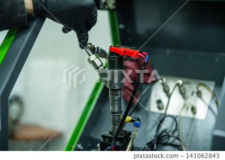 Technician hand connecting high pressure fuel pipe to common rail diesel injector on testing bench in repair workshop Technician hand connecting high pressure fuel pipe to common rail diesel injector on testing bench in repair workshop 141062843