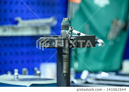 Common rail diesel fuel injector fixed in metal vice clamp holder on workshop table for disassembly and repair Common rail diesel fuel injector fixed in metal vice clamp holder on workshop table for disassembly and repair 141062844