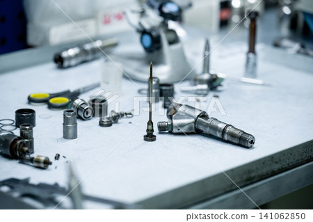 Disassembled used diesel fuel injector internal parts with wear signs on workbench table for inspection in repair workshop Disassembled used diesel fuel injector internal parts with wear signs on workbench table for inspection in repair workshop 141062850