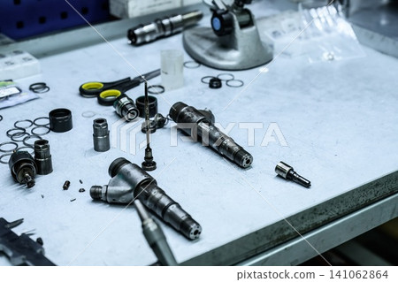 Disassembled old dirty used common rail fuel injector parts and internal components on workshop workbench table for repair 141062864