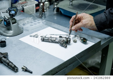 Mechanic hand using tweezers for small internal part installation during diesel fuel injector repair in workshop Mechanic hand using tweezers for small internal part installation during diesel fuel injector repair in workshop 141062869