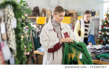 Adult woman chooses sweater in clothing store Adult woman chooses sweater in clothing store 141064167