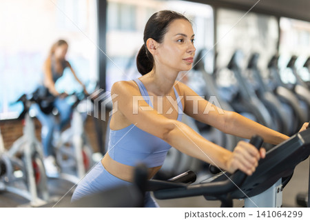Smiling young girl doing spin bike exercises in well-equipped gym 141064299