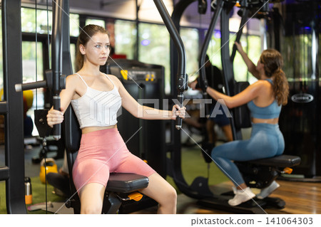 Sportive young girl training on chest fly machine in gym Sportive young girl training on chest fly machine in gym 141064303