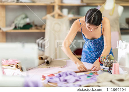 Young female seamstress attaching template to fabric 141064304