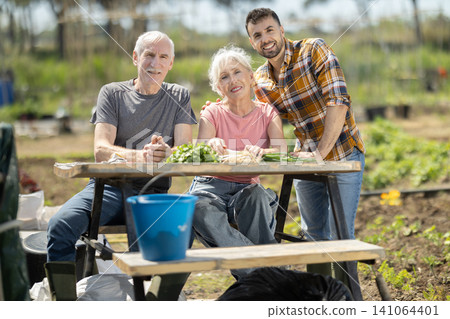 Young man and elderly couple sitting at table with harvest on field Young man and elderly couple sitting at table with harvest on field 141064401