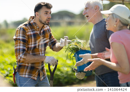 Mature couple and man argue with each other while standing near fence on small farm Mature couple and man argue with each other while standing near fence on small farm 141064424