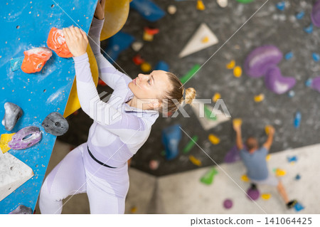 Adult woman practicing rock climbing on climbing wall Adult woman practicing rock climbing on climbing wall 141064425