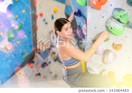 Cheerful young girl climbing artificial wall in bouldering center 141064483