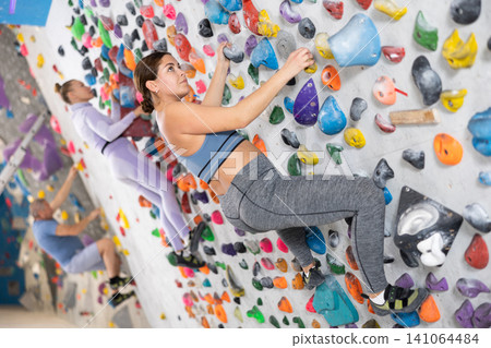 Young female alpinist practicing indoor a rock-climbing on a artificial boulder without safety belts Young female alpinist practicing indoor a rock-climbing on a artificial boulder without safety belts 141064484
