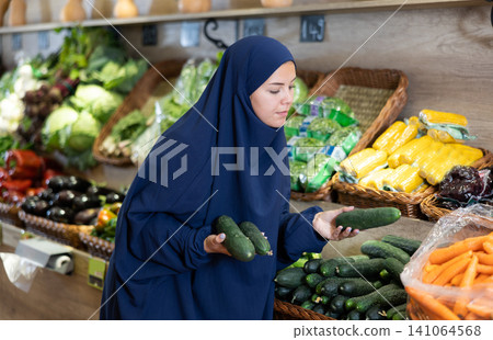 Woman in a veil buys ripe cucumbers in supermarket Woman in a veil buys ripe cucumbers in supermarket 141064568