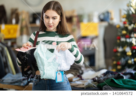 Young woman choosing panty sets on Christmas tree background in clothing store Young woman choosing panty sets on Christmas tree background in clothing store 141064572
