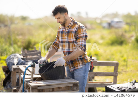 Young man filling bucket with water for field irrigation Young man filling bucket with water for field irrigation 141064579