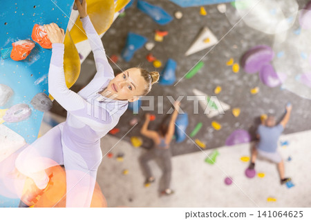 Adult woman practicing rock climbing on climbing wall Adult woman practicing rock climbing on climbing wall 141064625