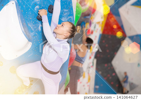 Adult woman practicing rock climbing on climbing wall Adult woman practicing rock climbing on climbing wall 141064627