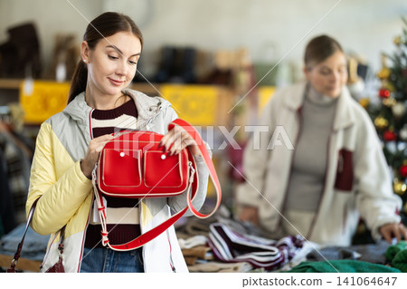 Positive young woman choosing handbag in clothing store 141064647