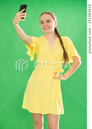 Teenage girl taking selfie in front of green screen Teenage girl taking selfie in front of green screen 141064658