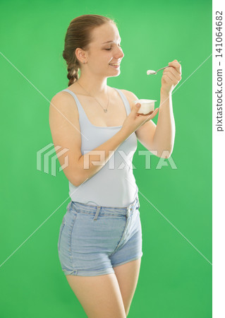 fit woman in casual clothes eating delicious sugar free yogurt on chromakey background 141064682