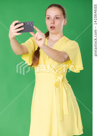 Teenage girl scans a barcode, she is standing in a yellow dress against a chroma key Teenage girl scans a barcode, she is standing in a yellow dress against a chroma key 141064688
