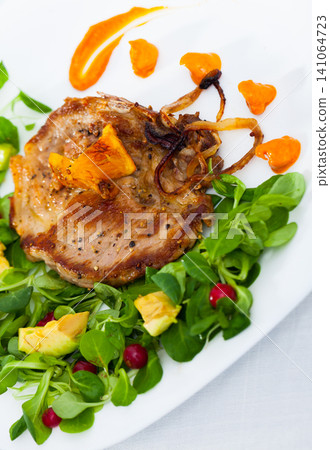 Cooked fried pork meat with herbs, sauce and berries on plate 141064723