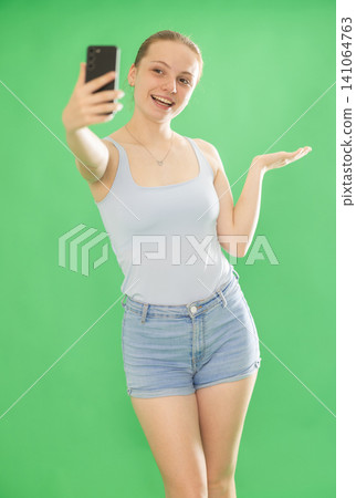 Teenage girl in blue top takes selfie on a smartphone on green background. Chroma key compositing Teenage girl in blue top takes selfie on a smartphone on green background. Chroma key compositing 141064763