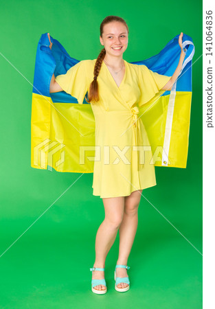 Teenage girl in yellow dress with large flag of Ukraine posing on green background. Chroma key compositing Teenage girl in yellow dress with large flag of Ukraine posing on green background. Chroma key compositing 141064836