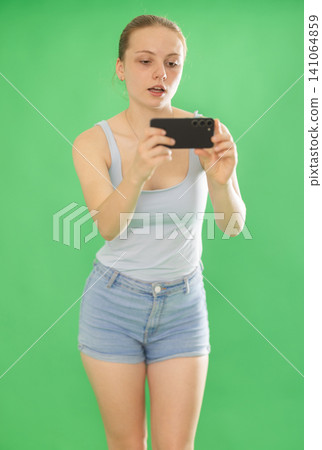 Teenage girl in blue top takes photo or scans QR code with a smartphone. Chroma key compositing Teenage girl in blue top takes photo or scans QR code with a smartphone. Chroma key compositing 141064859