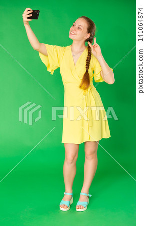 Teenage girl taking selfie in front of green screen Teenage girl taking selfie in front of green screen 141064874