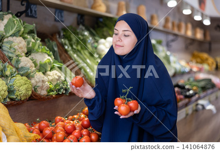Delighted young Muslim woman purchaser choosing tomatos in grocery store Delighted young Muslim woman purchaser choosing tomatos in grocery store 141064876