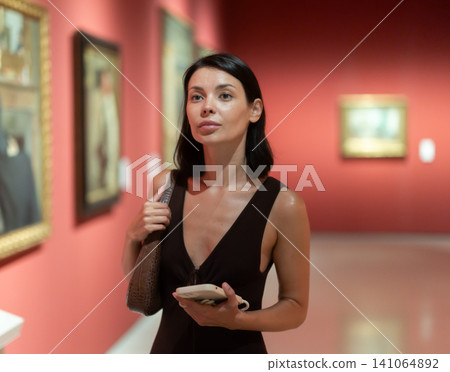Woman with phone in hands in museum hall, view painting exhibition 141064892