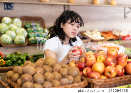 Happy smiling girl making purchases in supermarket, choosing fresh apples Happy smiling girl making purchases in supermarket, choosing fresh apples 141064988