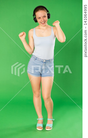 Young woman in casual clothes listens to music in modern headphones Young woman in casual clothes listens to music in modern headphones 141064995