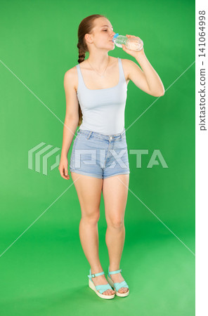 Teenage girl drinking water in front of green screen Teenage girl drinking water in front of green screen 141064998