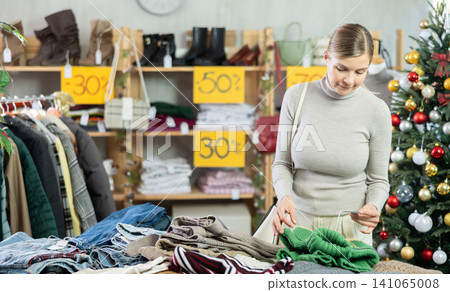 Woman client looks at products in store, choose closely warm sweater Woman client looks at products in store, choose closely warm sweater 141065008