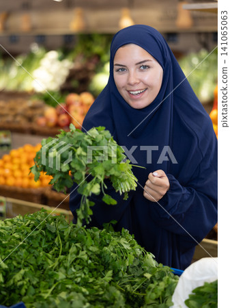 Young european woman in islamic dress choosing greens at market 141065063