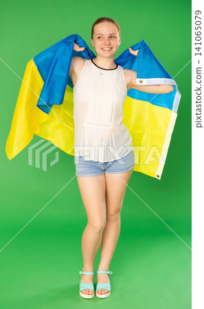 Teenage girl in white blouse with large flag of Ukraine posing on green background. Chroma key compositing Teenage girl in white blouse with large flag of Ukraine posing on green background. Chroma key compositing 141065079