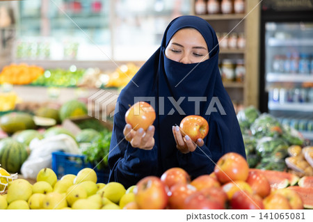 Delighted young Muslim woman purchaser choosing apples in grocery store Delighted young Muslim woman purchaser choosing apples in grocery store 141065081