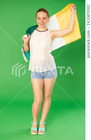 Teenage girl in white blouse with large flag of Ireland posing on green background. Chroma key compositing Teenage girl in white blouse with large flag of Ireland posing on green background. Chroma key compositing 141065082