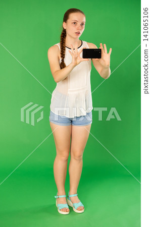 Teenage girl taking photo or scanning QR code in front of green screen Teenage girl taking photo or scanning QR code in front of green screen 141065106