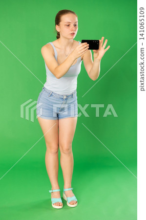 Teenage girl taking photo or scanning QR code in front of green screen Teenage girl taking photo or scanning QR code in front of green screen 141065109