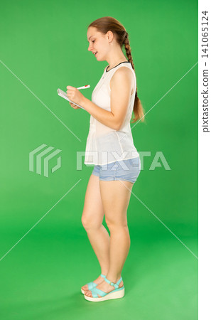 Teenage girl writing in notebook with pen in front of green screen Teenage girl writing in notebook with pen in front of green screen 141065124