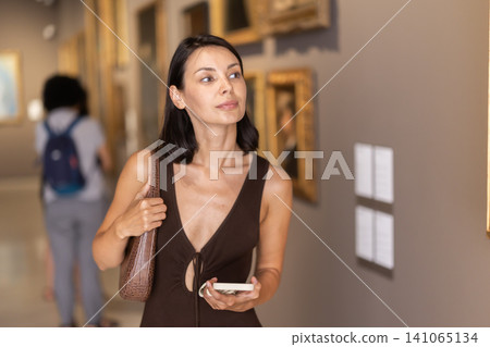 Woman visiting museum and looking at paintings in gold frames Woman visiting museum and looking at paintings in gold frames 141065134