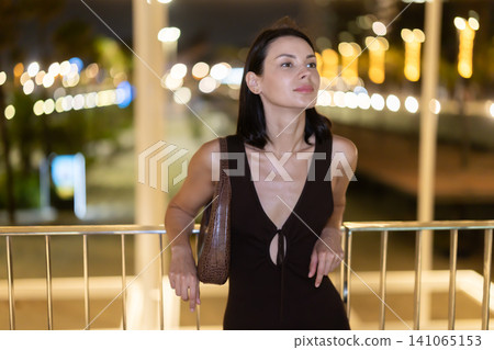 Young woman leaning on metal railing against background of blurred city lights Young woman leaning on metal railing against background of blurred city lights 141065153